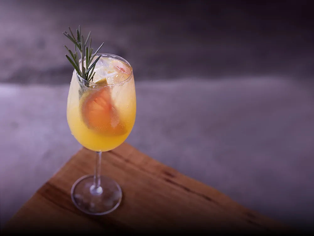 Cóctel Mango Tonic con mezcal artesanal Casa Xamu, rodaja de toronja y romero fresco, servido en copa. Mezcal 100% orgánico de cuarta generación de maestros mezcaleros de Santiago Matatlán, Oaxaca. Frescura tropical con espíritu de agave.