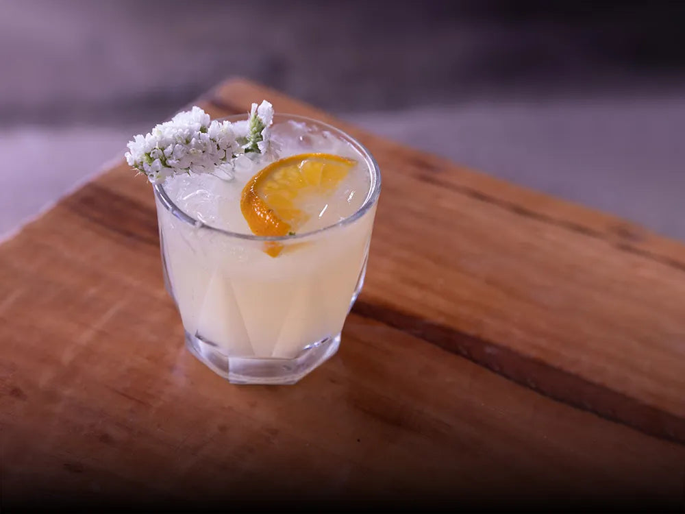 Cóctel Mula Xamu con mezcal artesanal Casa Xamu, hierbabuena, rodaja de naranja y flor blanca, servido en vaso old fashioned con hielo.