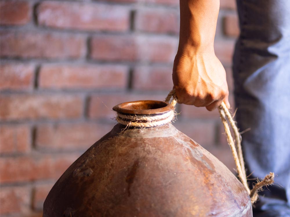 Jarro de barro utilizado en la destilación artesanal, sostenido por un trabajador con lazo de fibra natural.